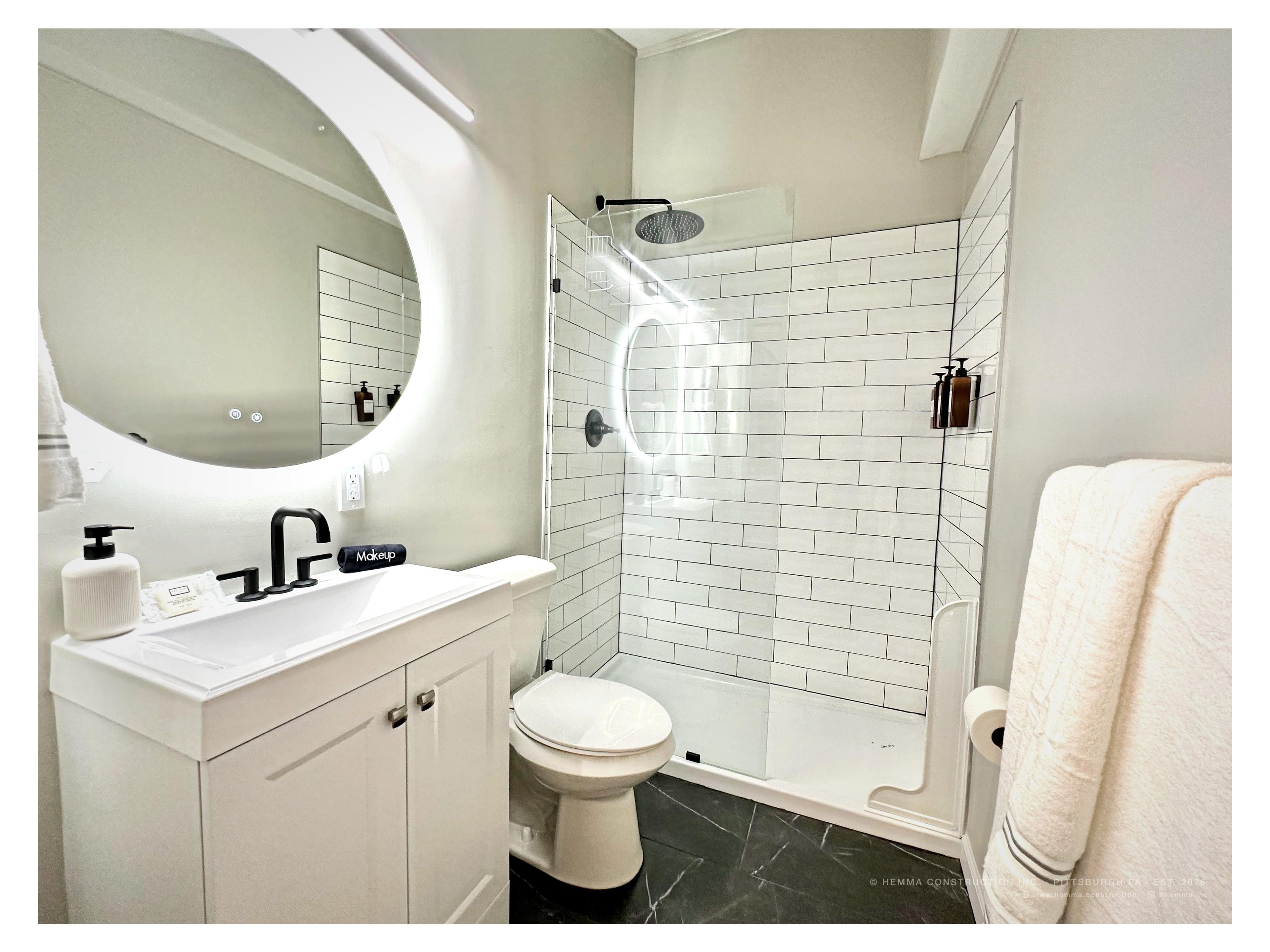 Bathroom with walk-in shower and backlit round mirror