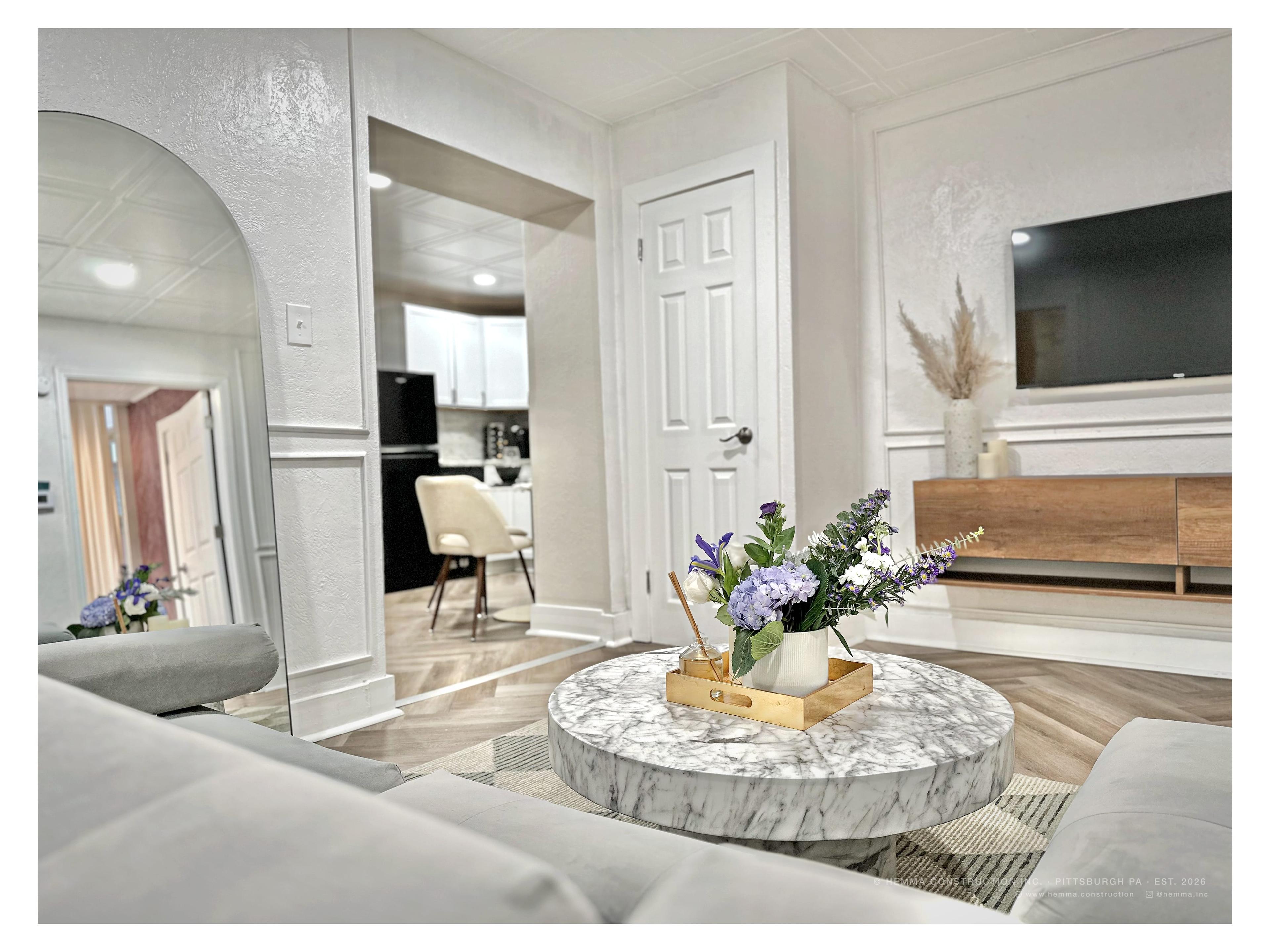 Living room — marble round coffee table, floral arrangement, arched mirror, kitchen beyond
