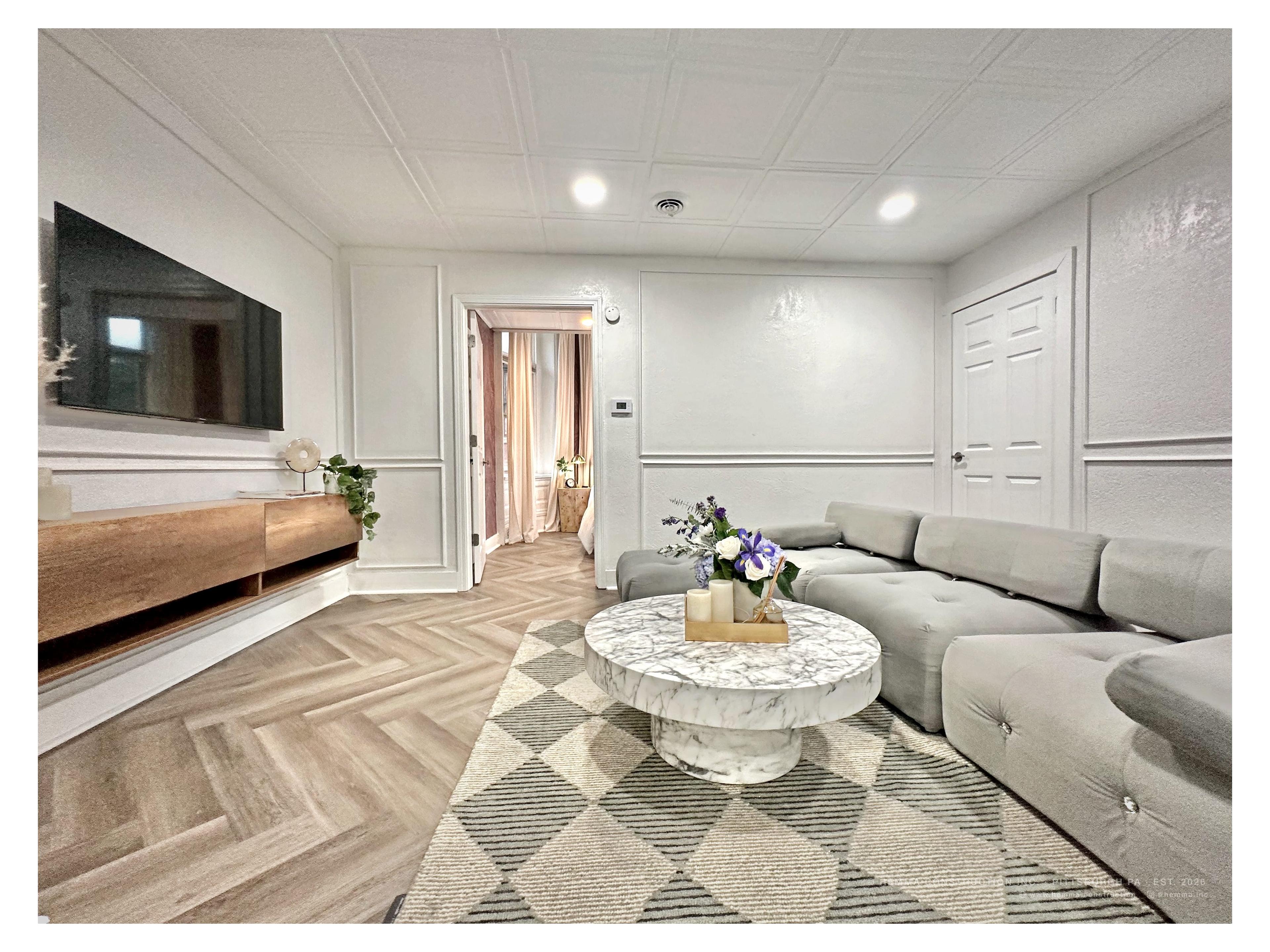 Living room full — gray sectional, marble coffee table, white wainscoting, herringbone floor