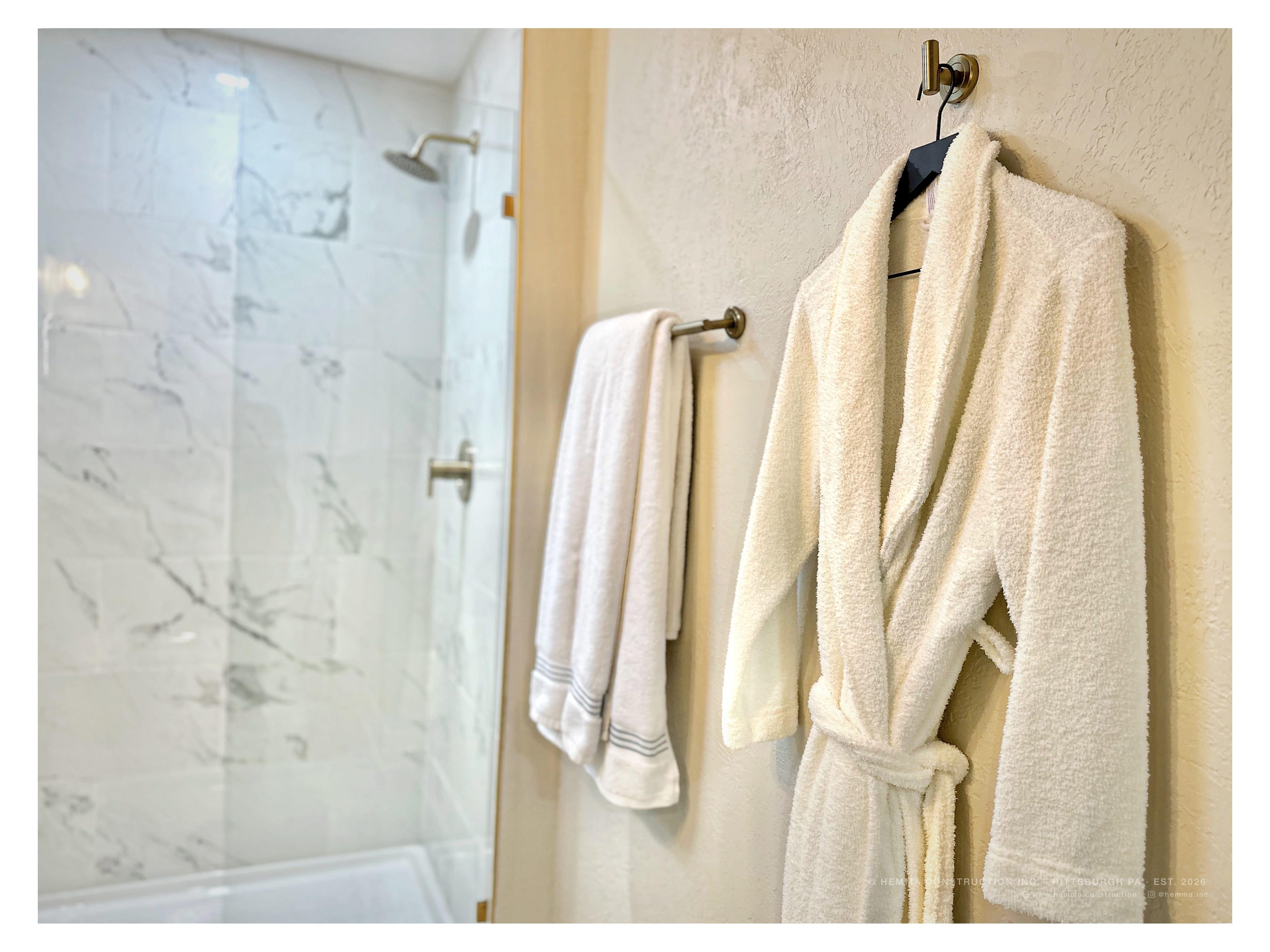 Bathroom — robe on hook, marble shower glass, gold hardware
