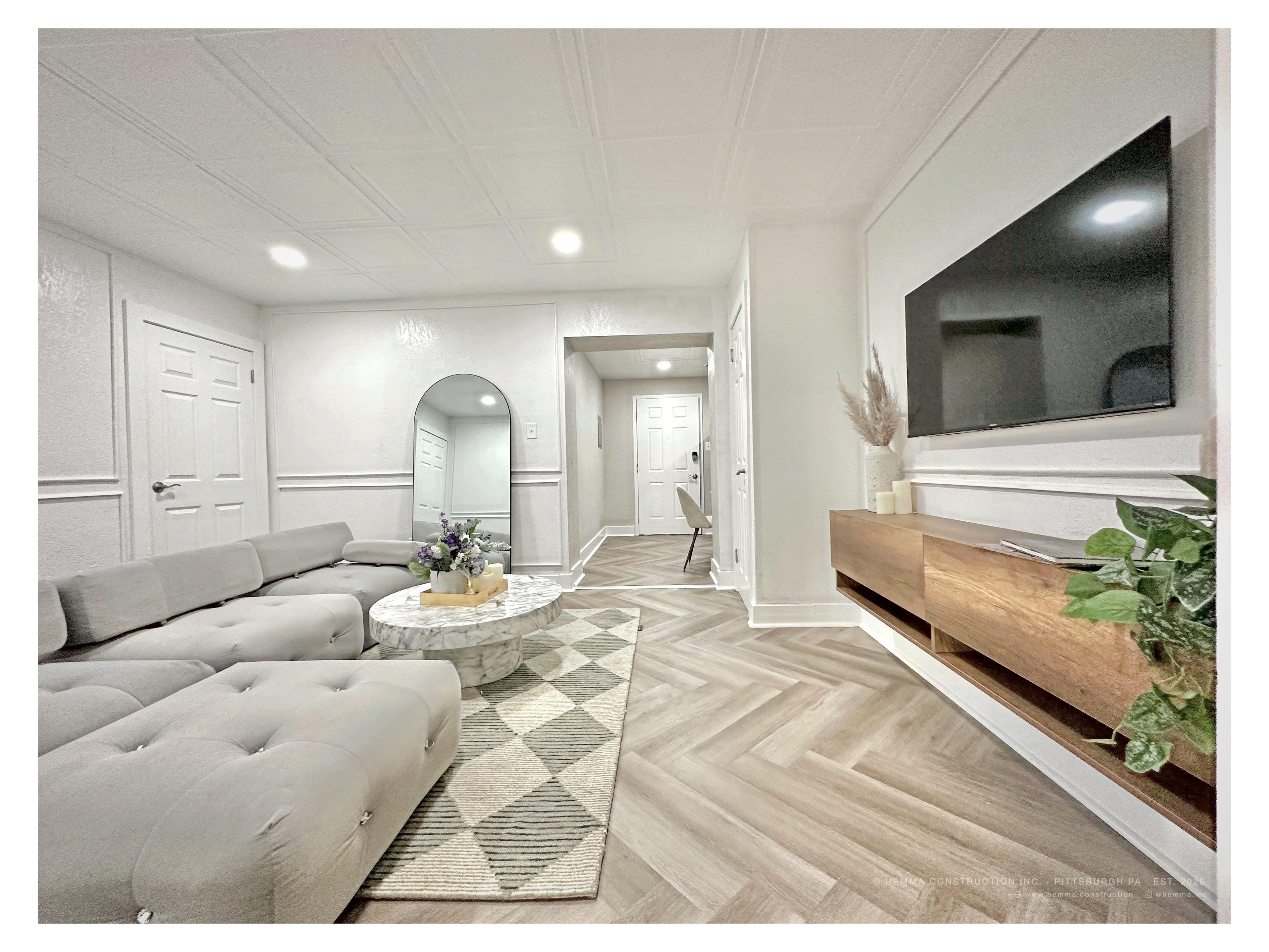 Living room wide — gray tufted sectional, arched floor mirror, herringbone floor