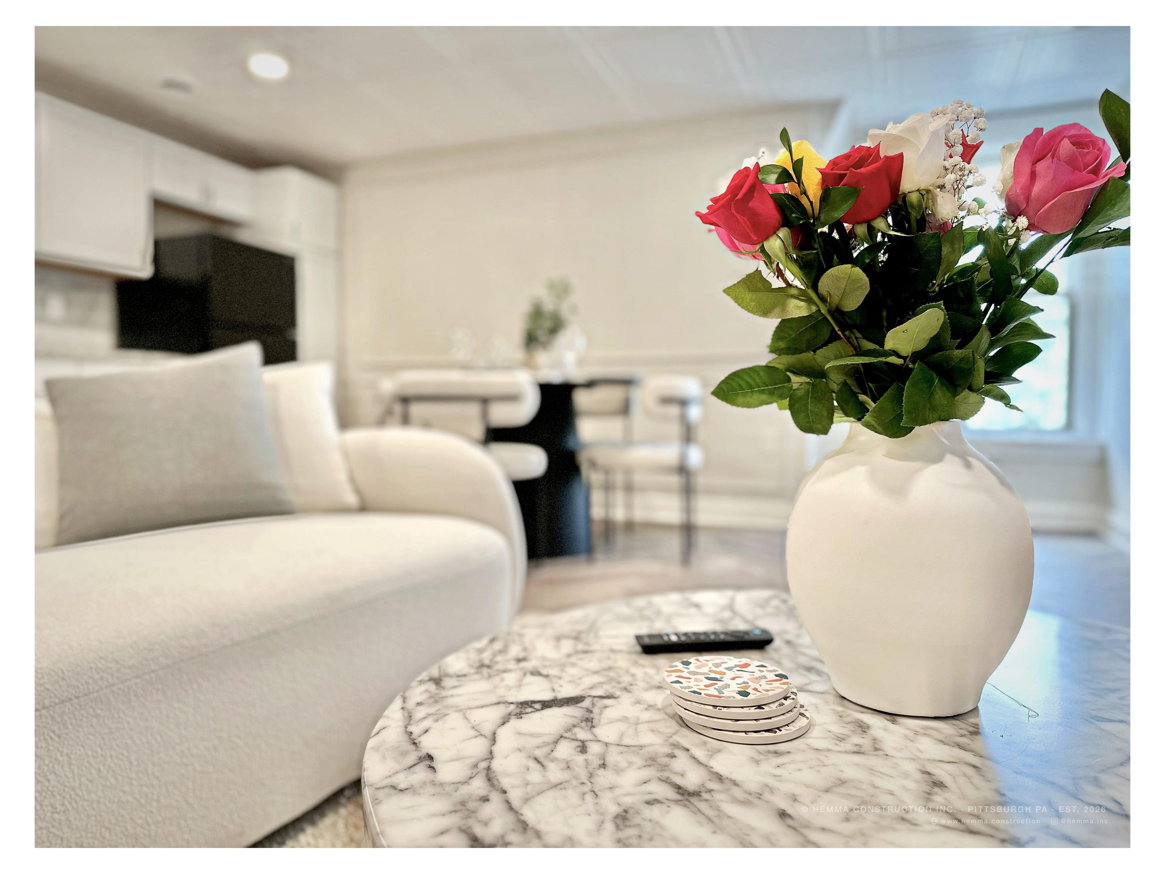 Living room detail — roses in white vase on marble coffee table, dining beyond