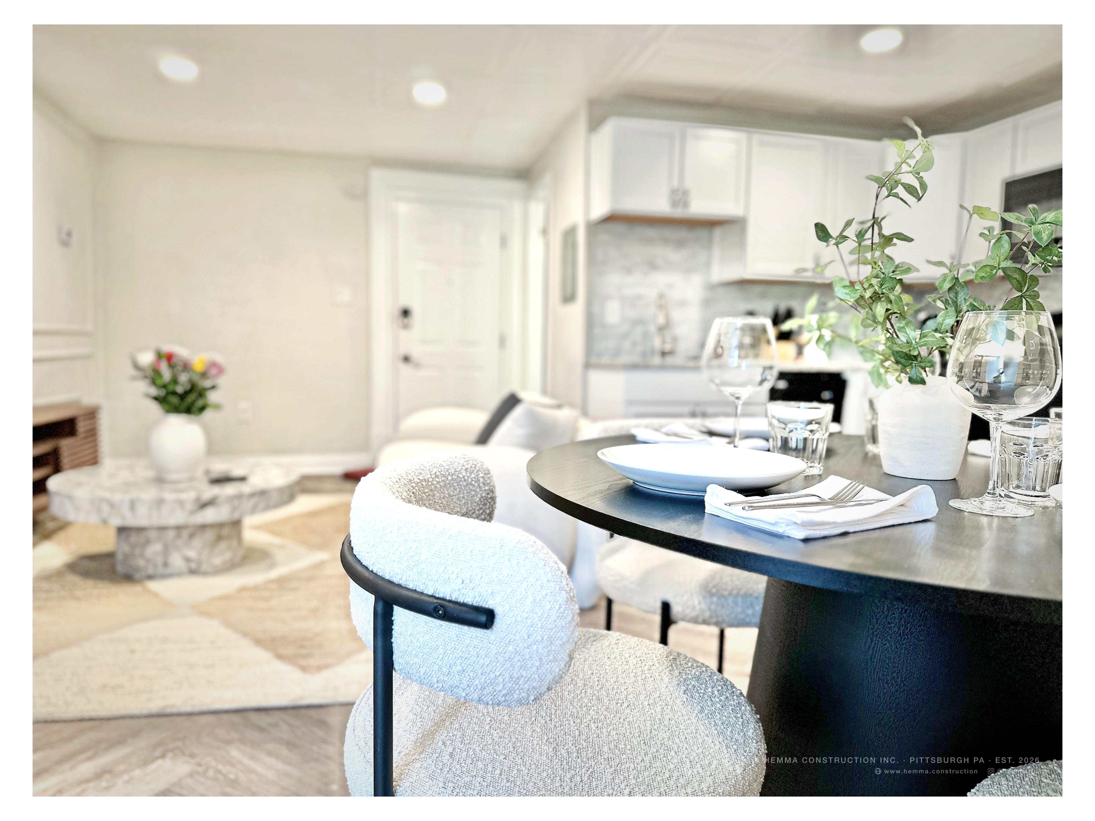 Dining table — white plates, wine glasses, green botanical arrangement, kitchen behind
