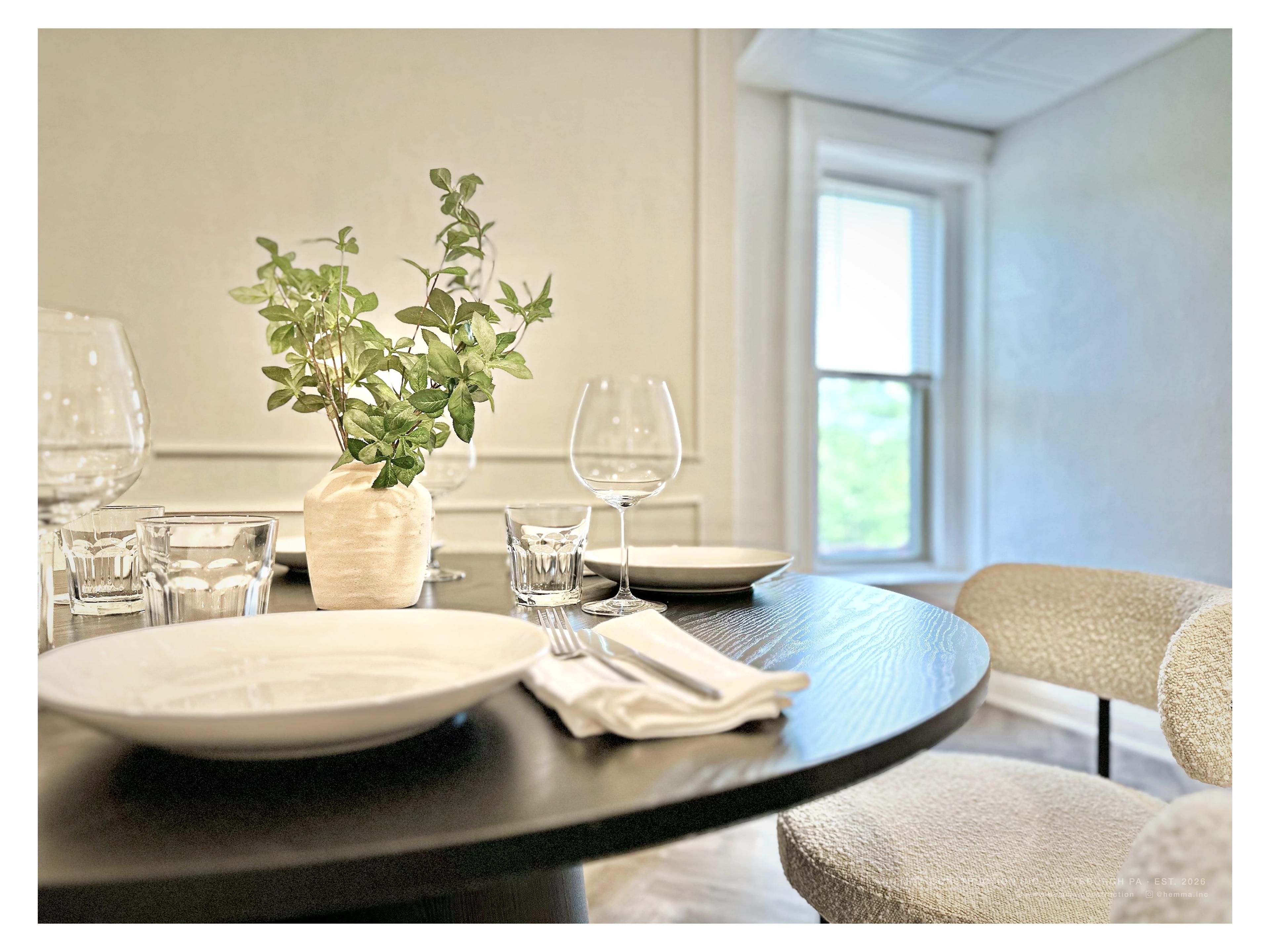 Dining table close-up — place settings, glassware, botanical arrangement, bay window