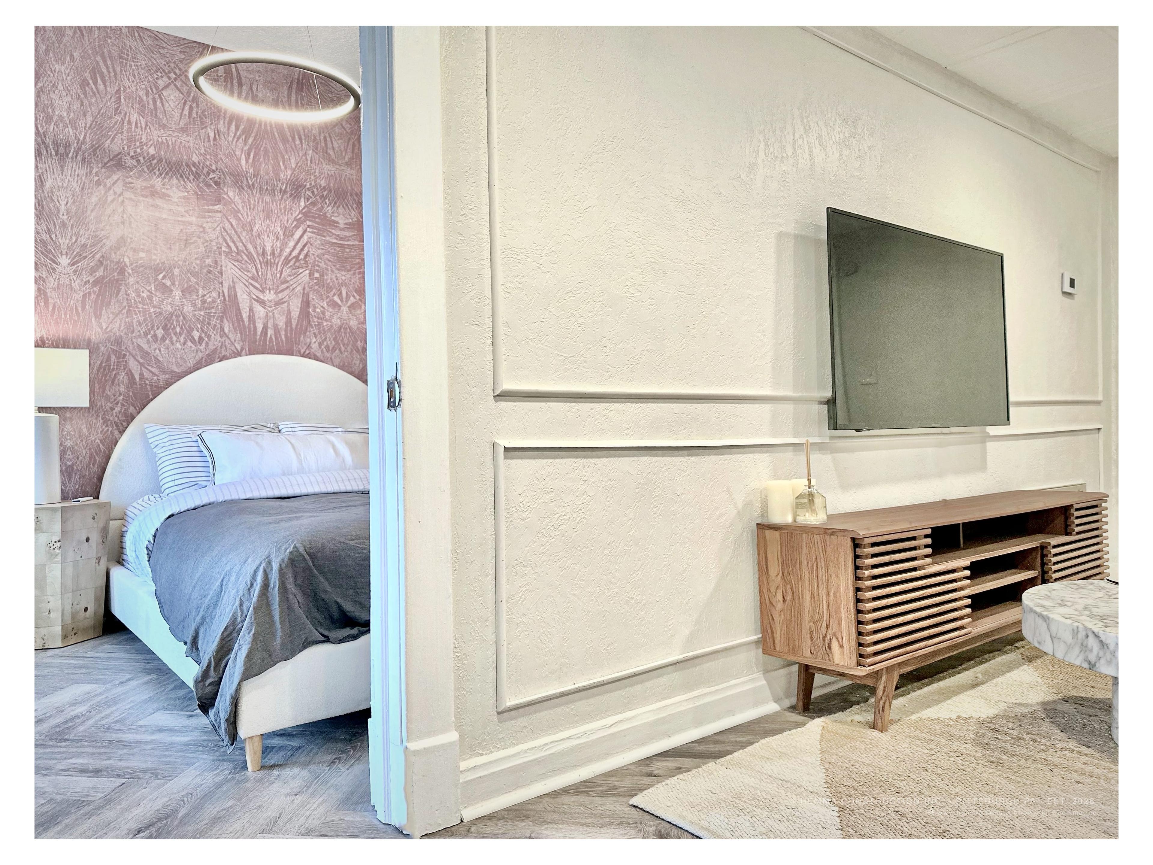 Living room and bedroom threshold — credenza with TV, pink bedroom visible through door