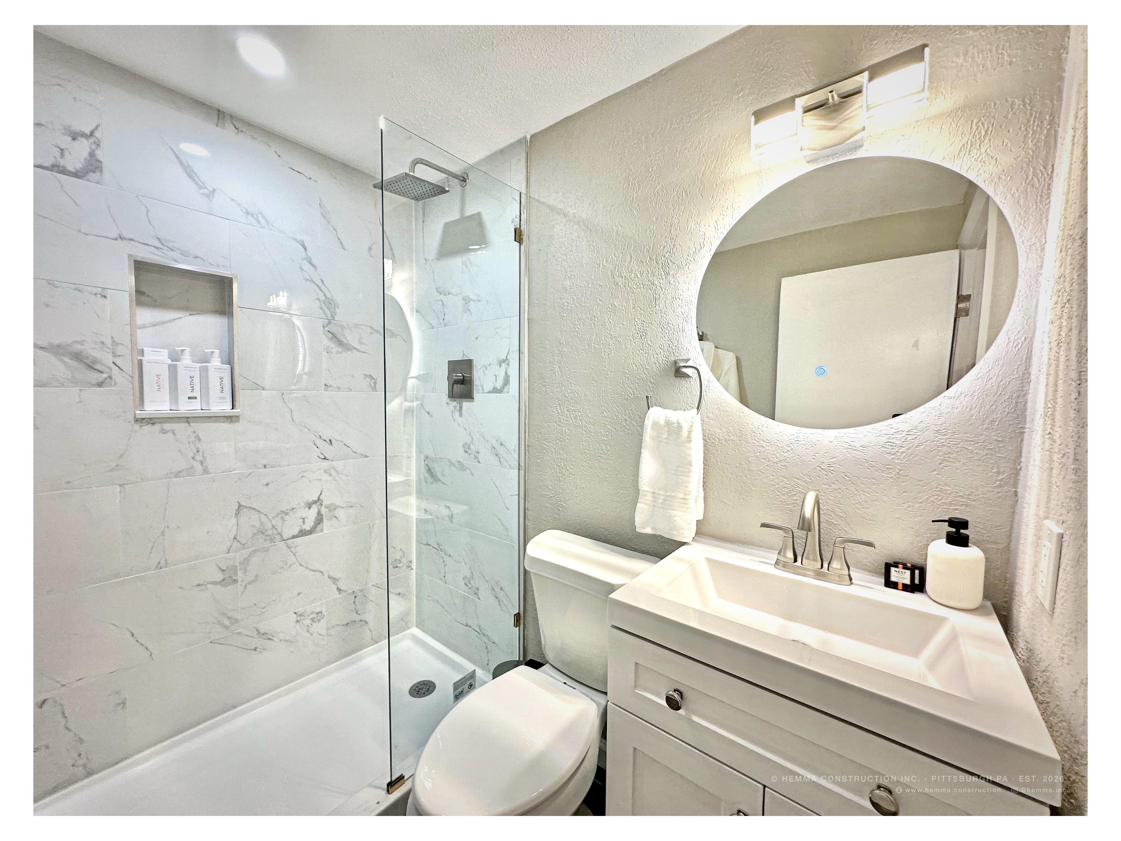 Bathroom — marble shower, round backlit mirror, white vanity, Nest amenities
