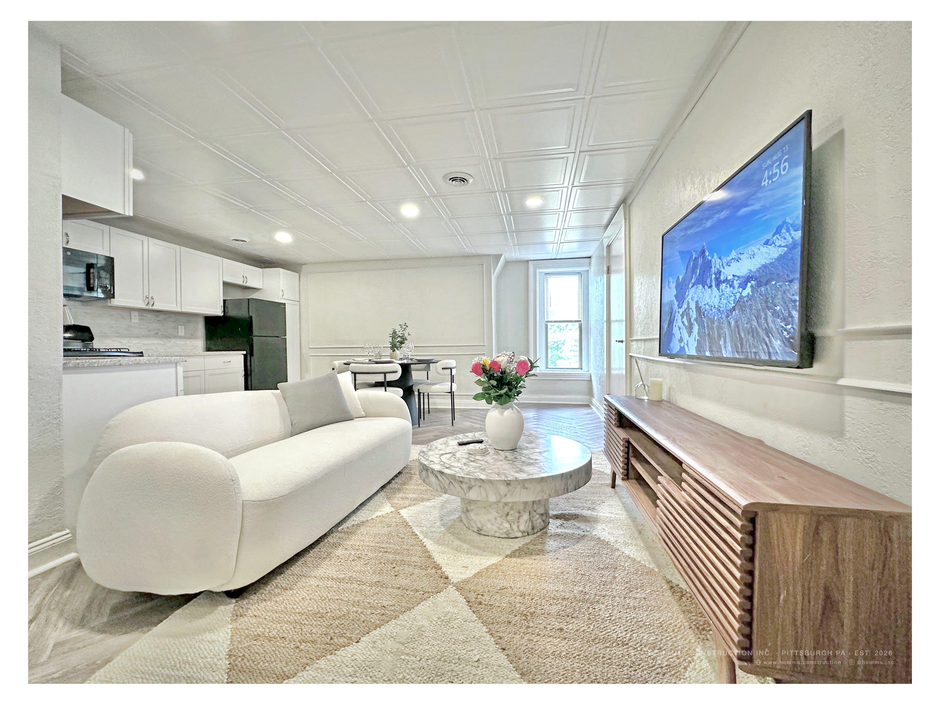 Living room wide — white sofa, marble table, dining area, credenza with TV