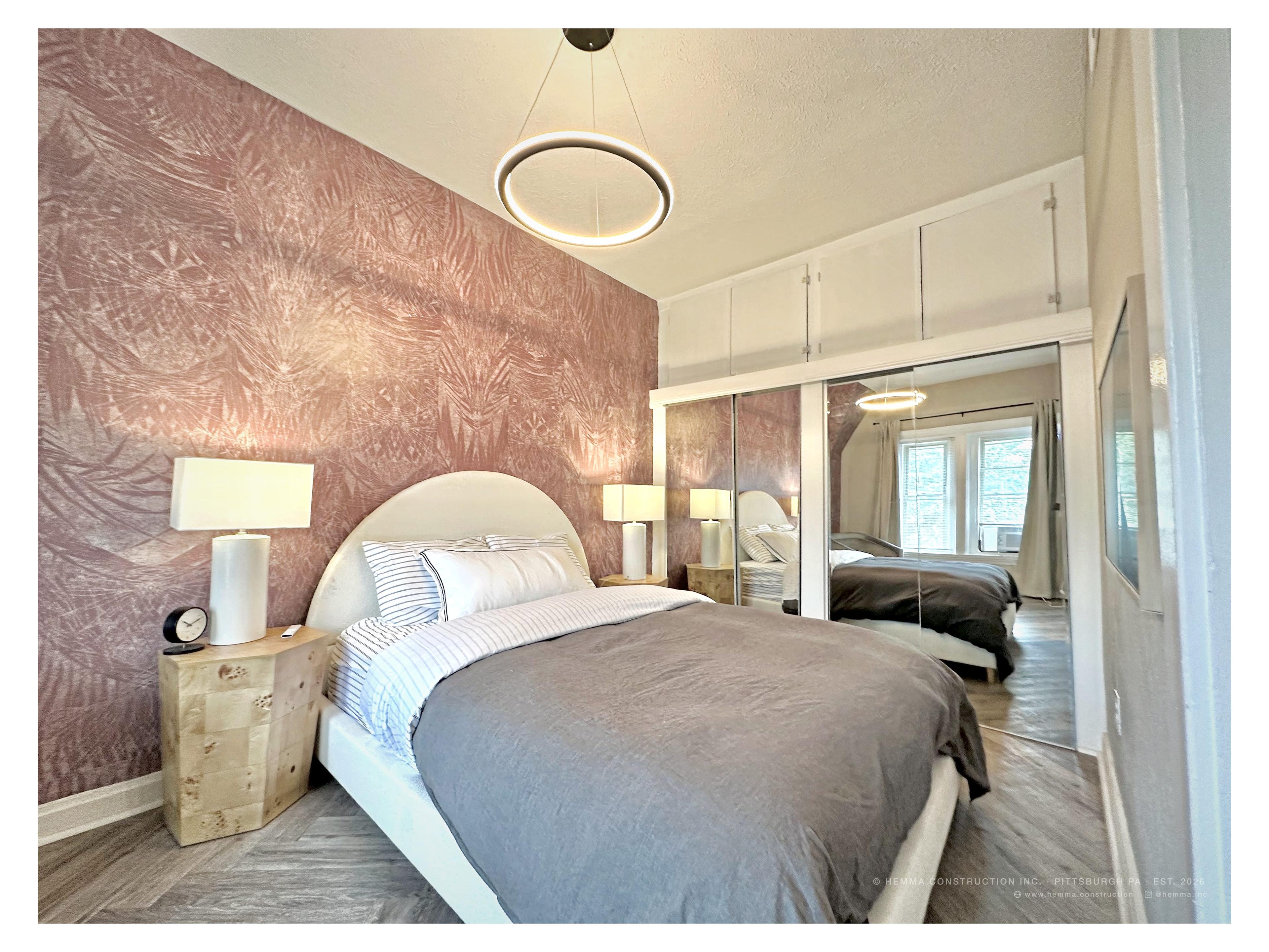 Unit 4 bedroom — arched headboard, pink botanical wallpaper, ring pendant, mirrored wardrobe, herringbone floor
